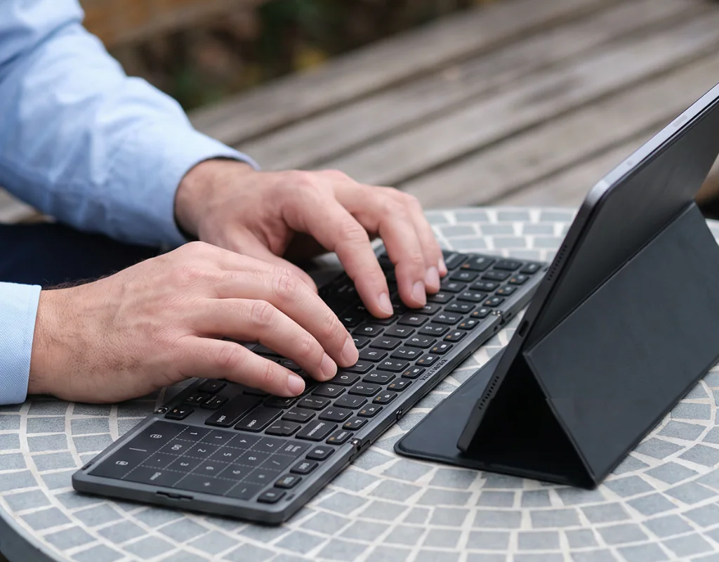 Hands using the Aimarz AF01 keyboard beside a tablet stand outdoors